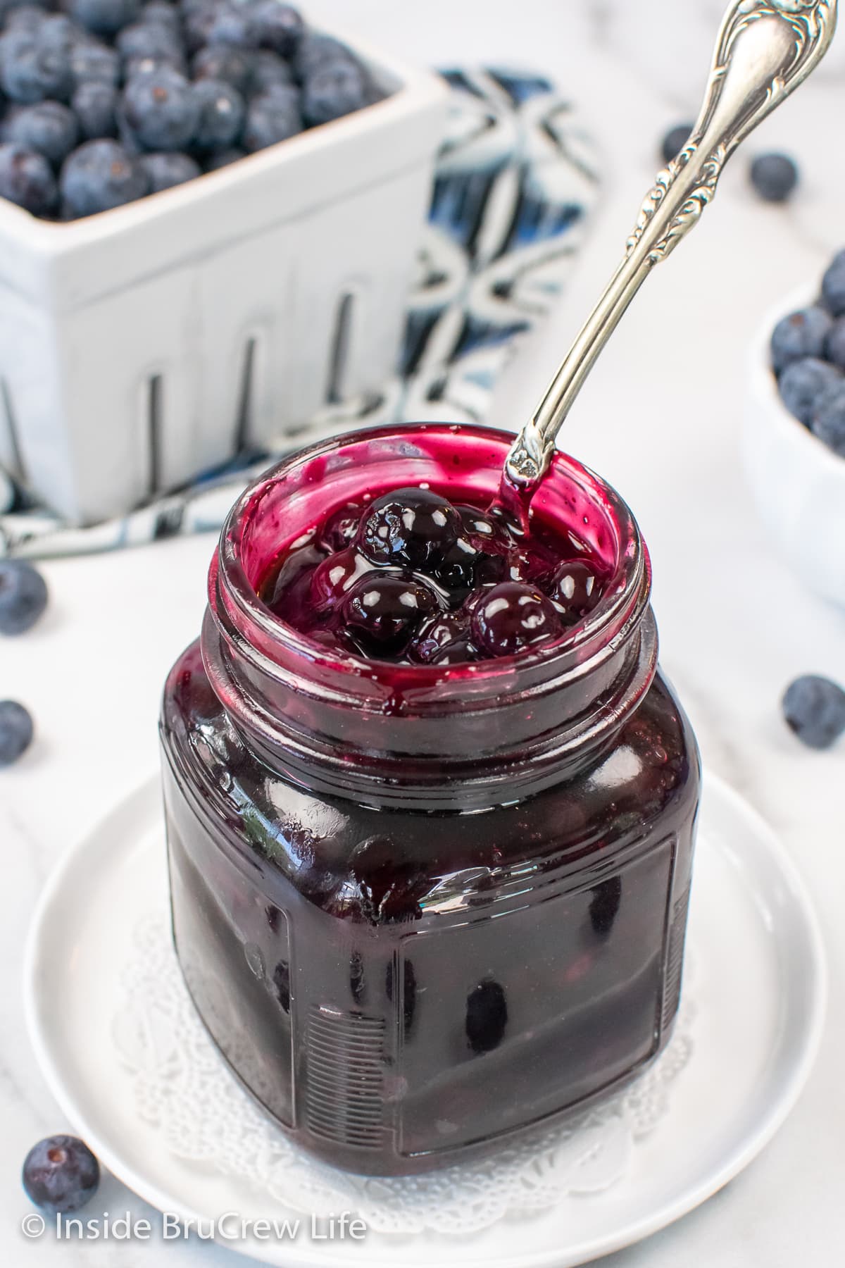 A clear jar filled with cooked blueberries and a spoon.