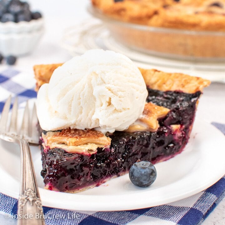 A slice of blueberry pie with ice cream on a white plate.
