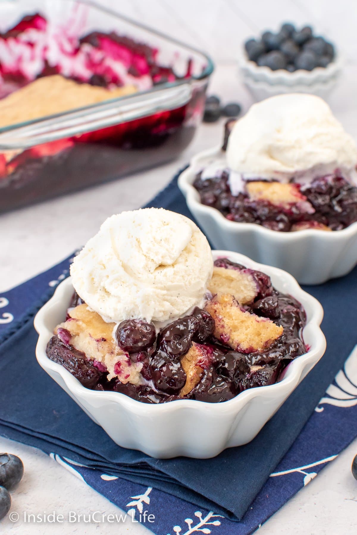 Two white bowls of fruit cobbler topped with ice cream.