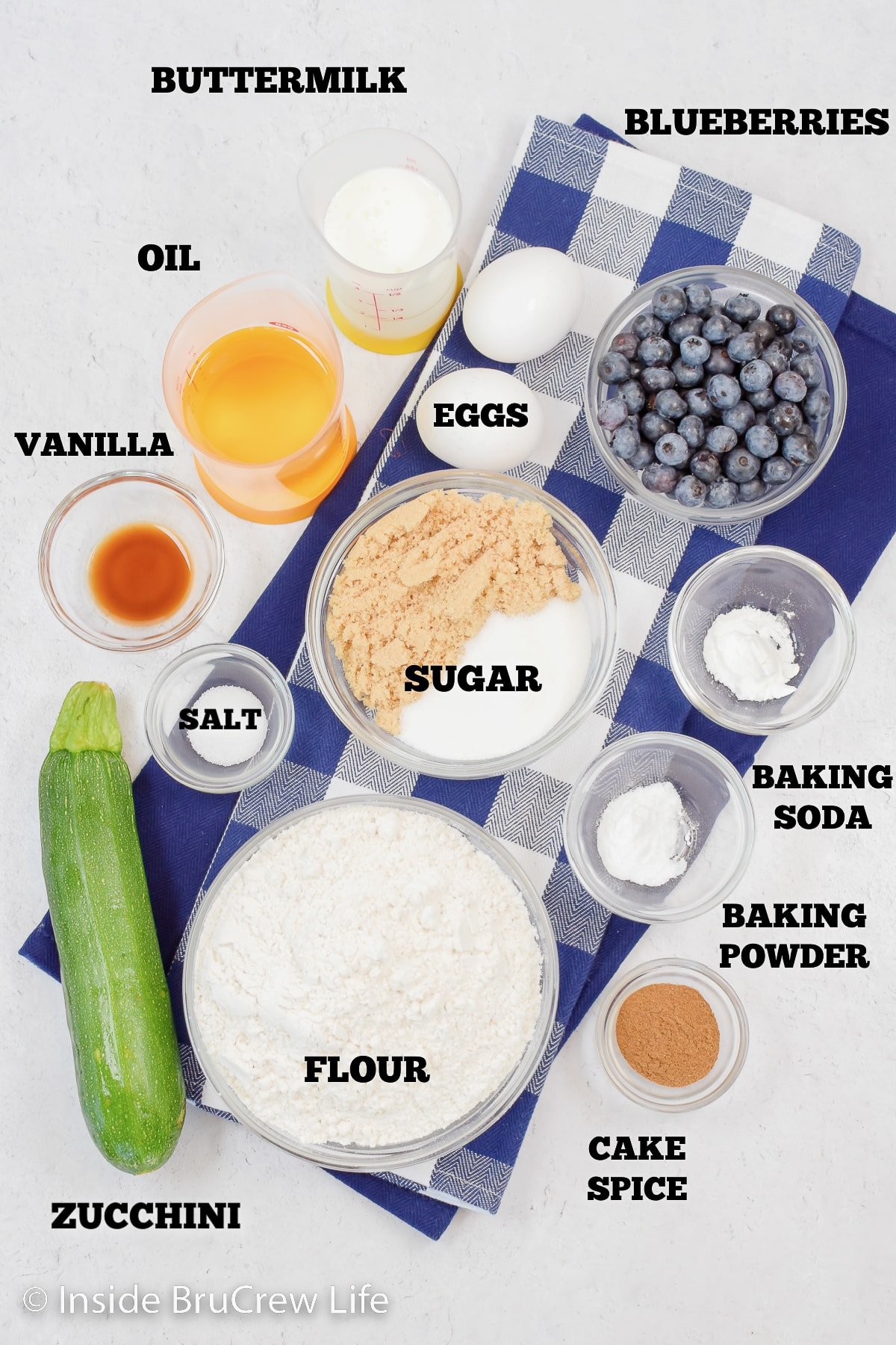 A white board with ingredients in bowls to make zucchini muffins.