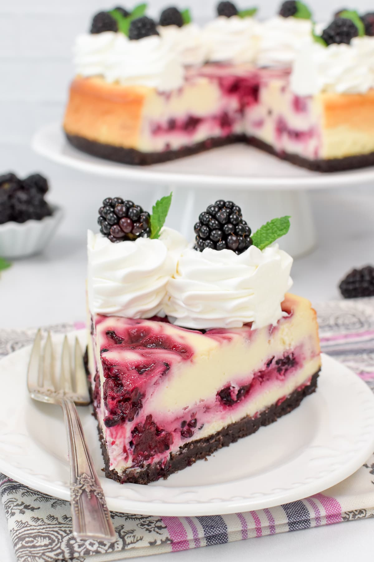 A slice of berry swirled cheesecake on a white plate.