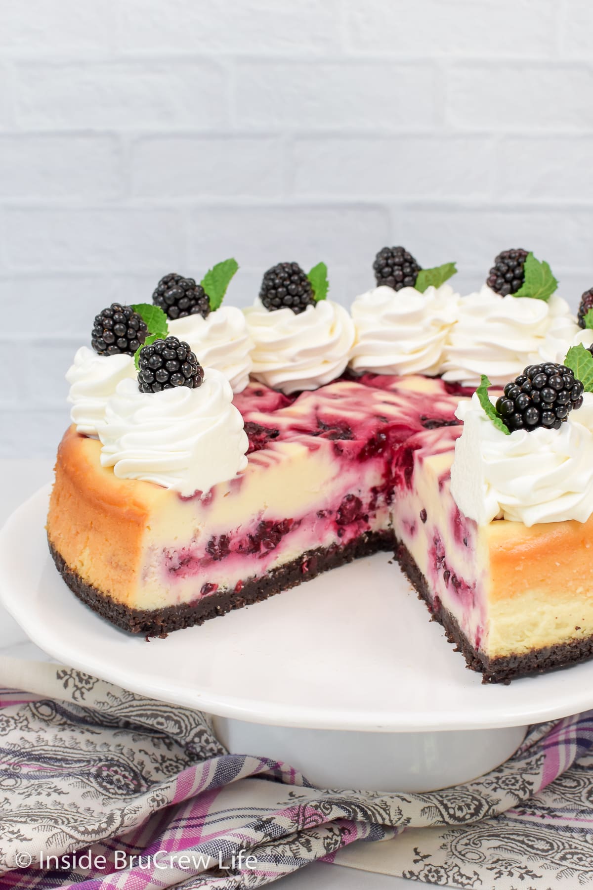 A full sized berry swirled cheesecake with a slice missing.