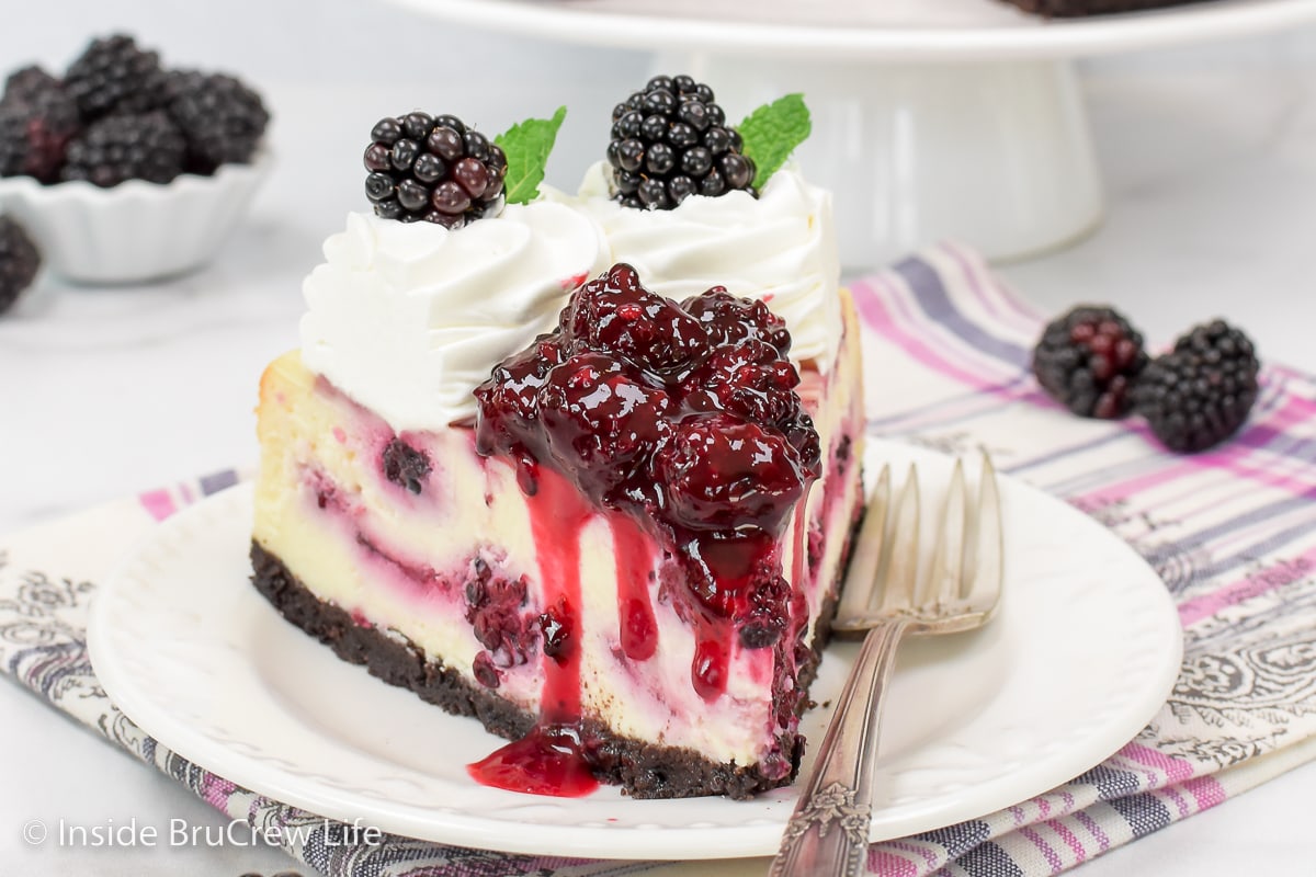 A white plate with a slice of cheesecake topped with berry pie filling on top.