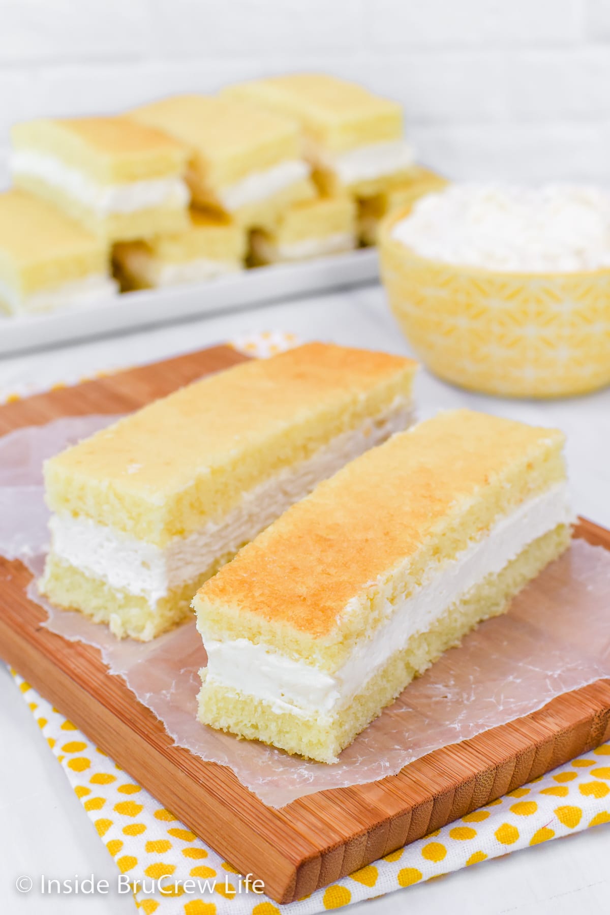 Two banana snack cakes with frosting on a wooden board.