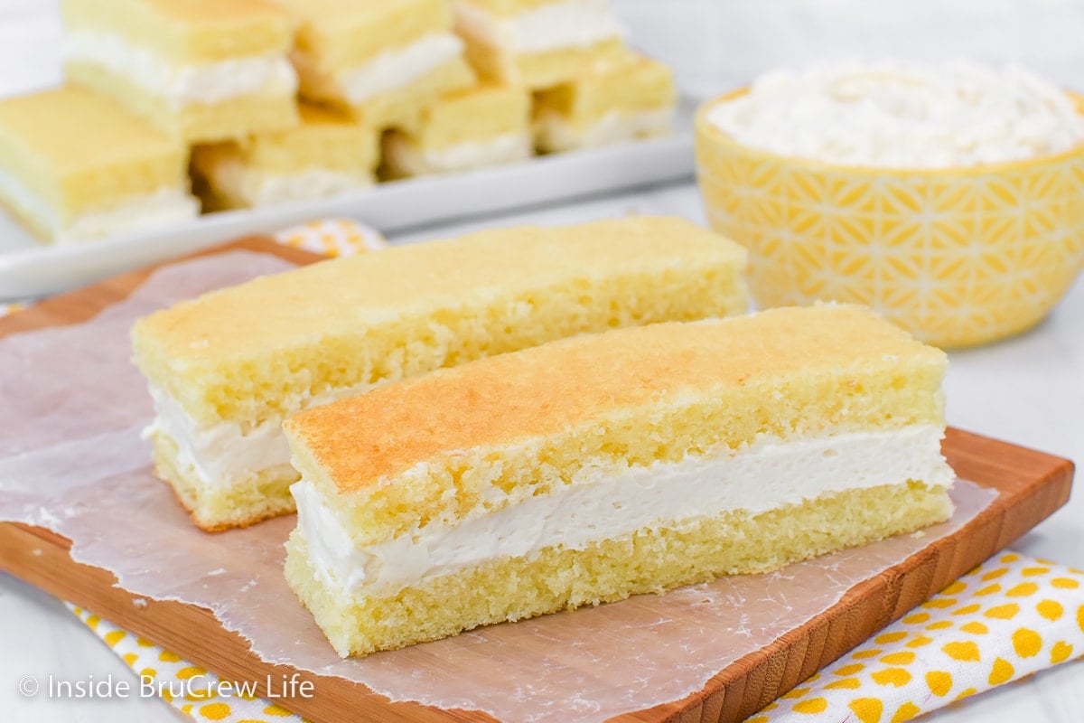 Two banana snack cakes with frosting on a wooden board.