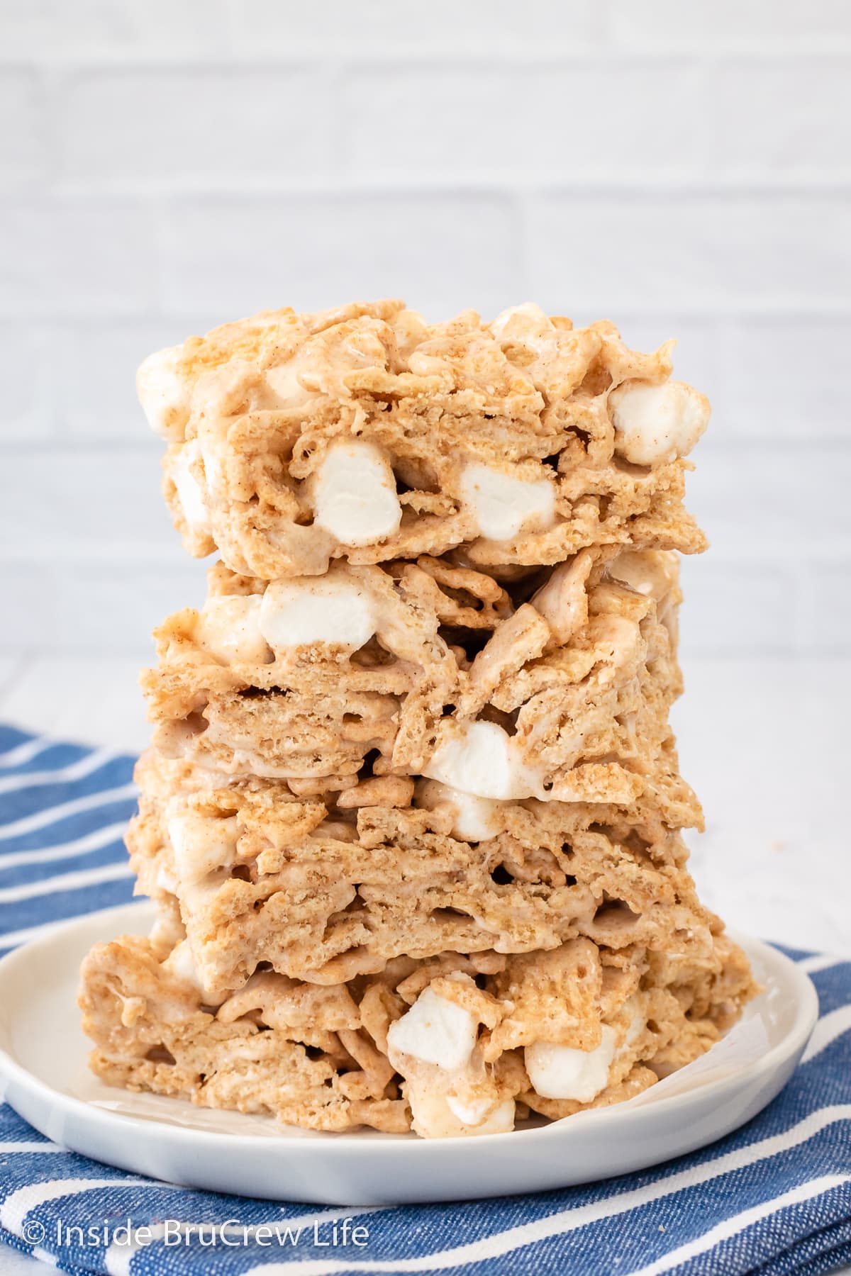 A stack of four marshmallow cereal treat bars on a white plate.