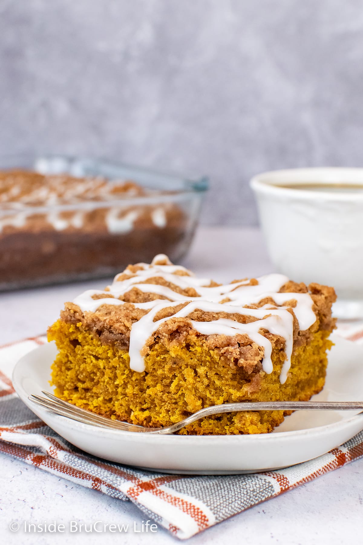 A slice of pumpkin cake topped with streusel and glaze on a white plate.