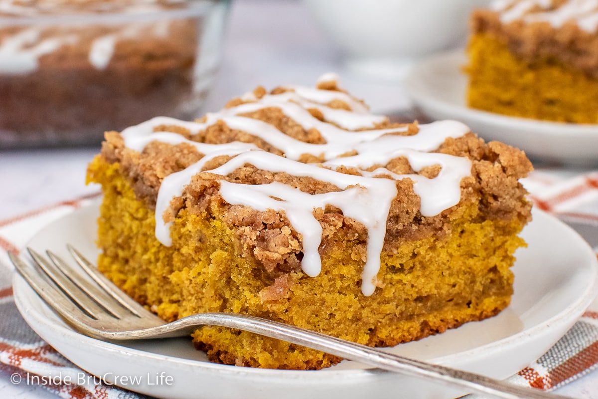 A white plate with a slice of pumpkin cake topped with streusel and glaze.