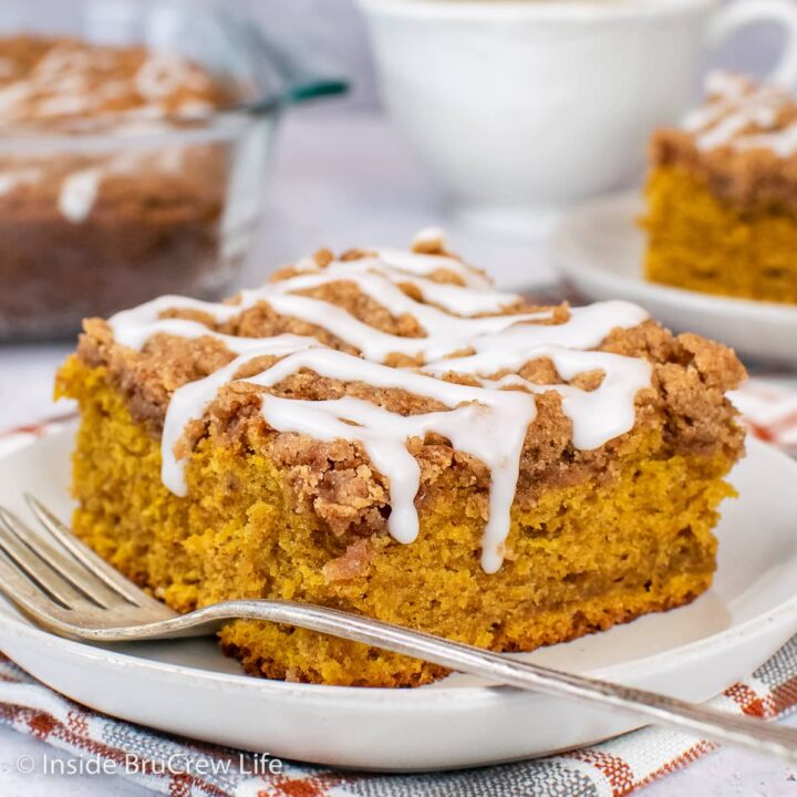 A white plate with a slice of pumpkin cake topped with streusel and glaze.