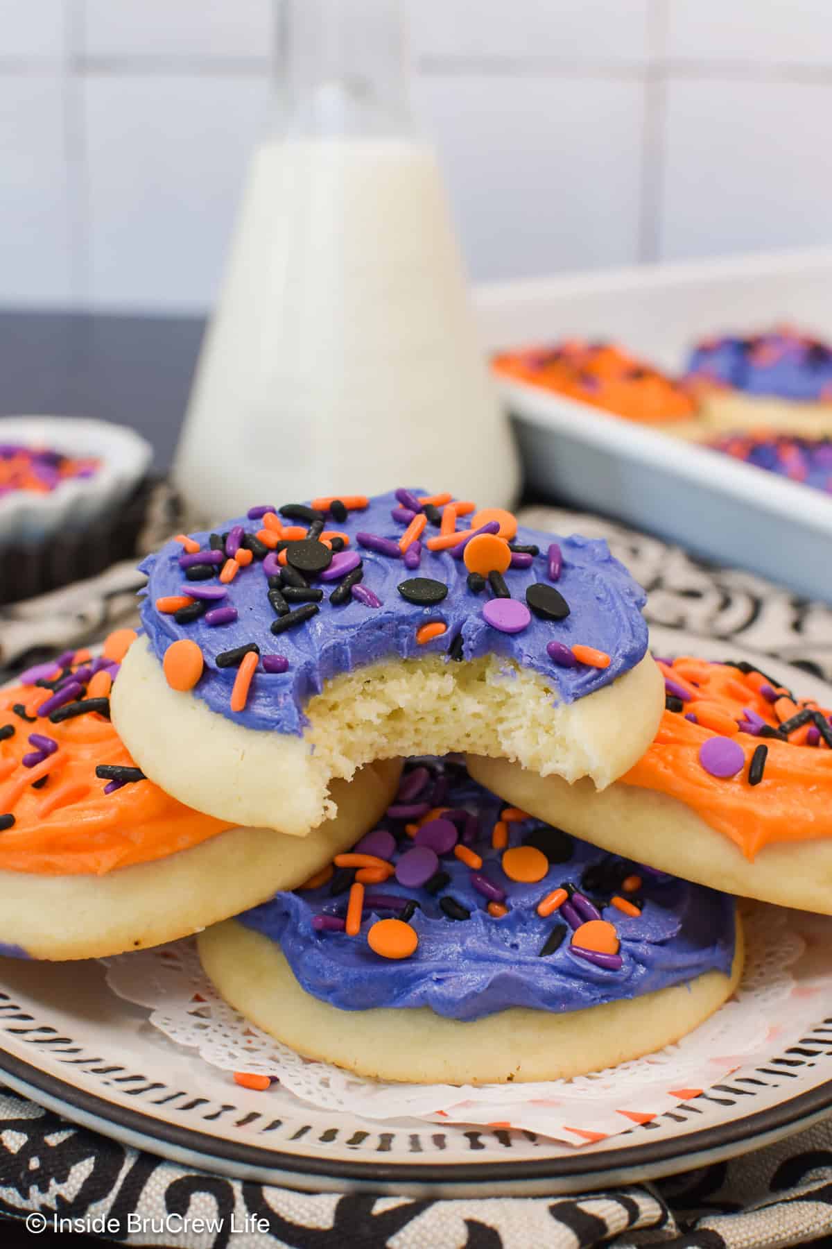 A stack of frosted sugar cookies on a plate with sprinkles.