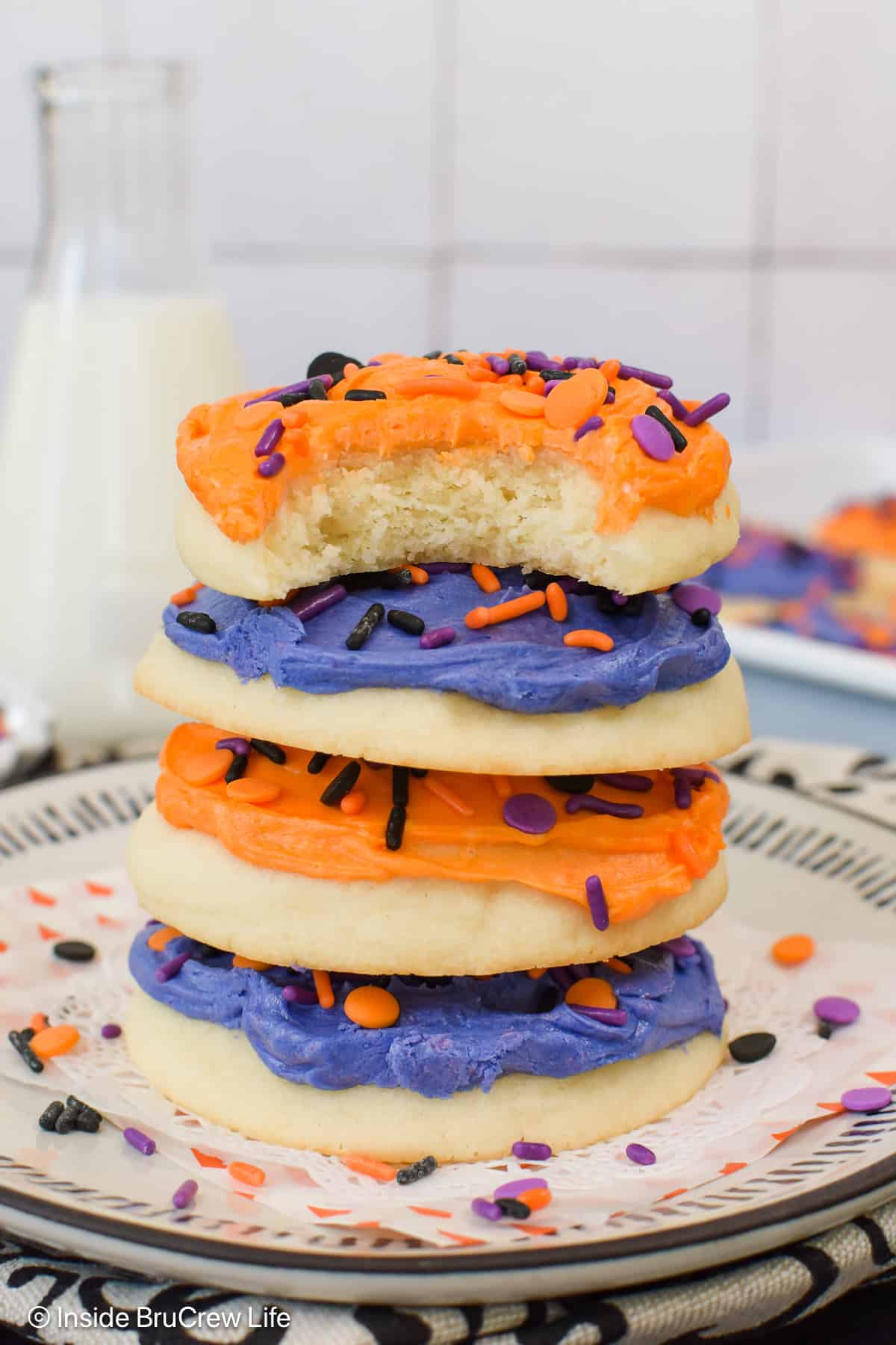 Four frosted sugar cookies stacked tall on a plate.