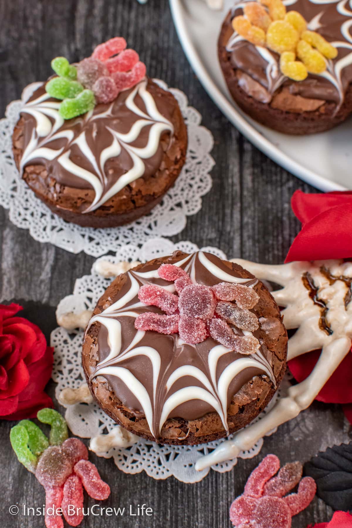 Two brownies topped with chocolate and spider gummies.