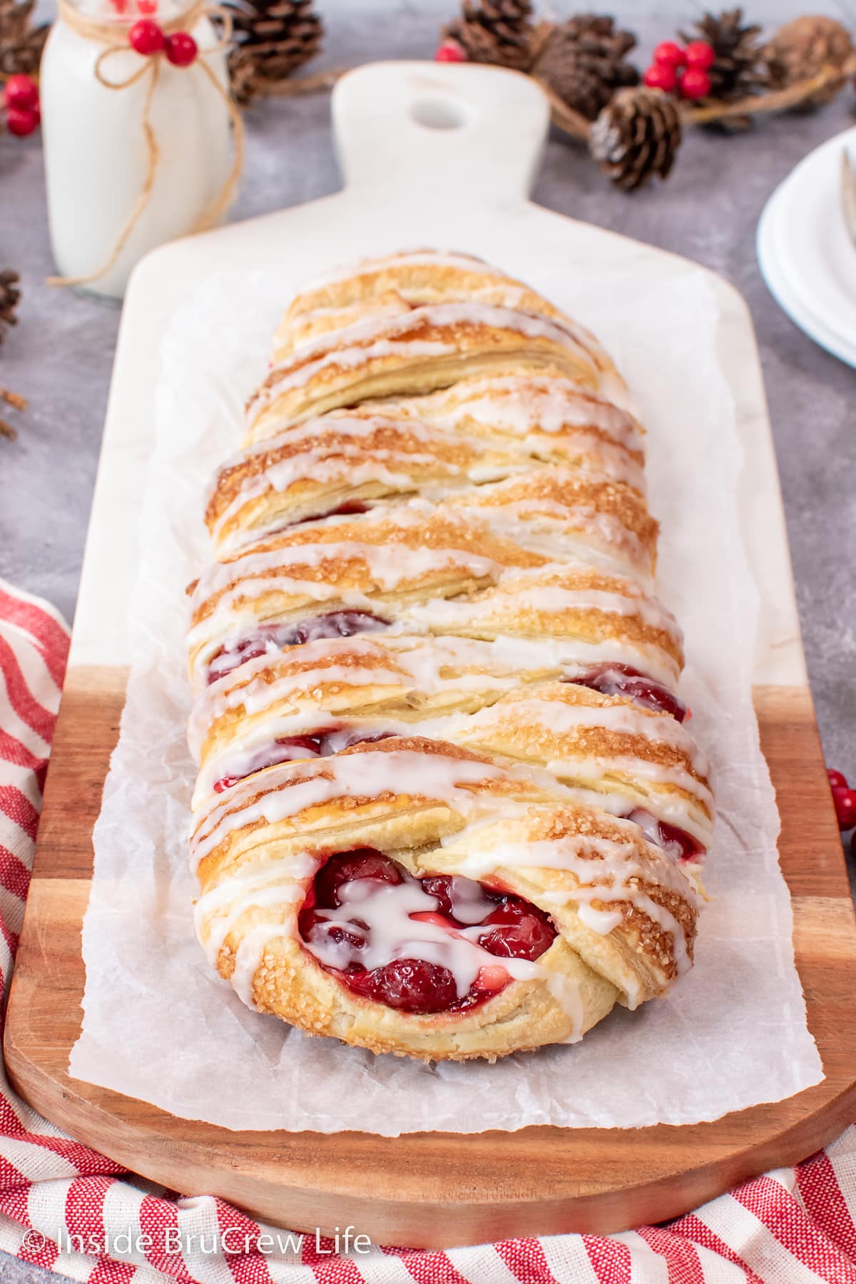 A full braided danish filled with cherry filling on a wooden board.
