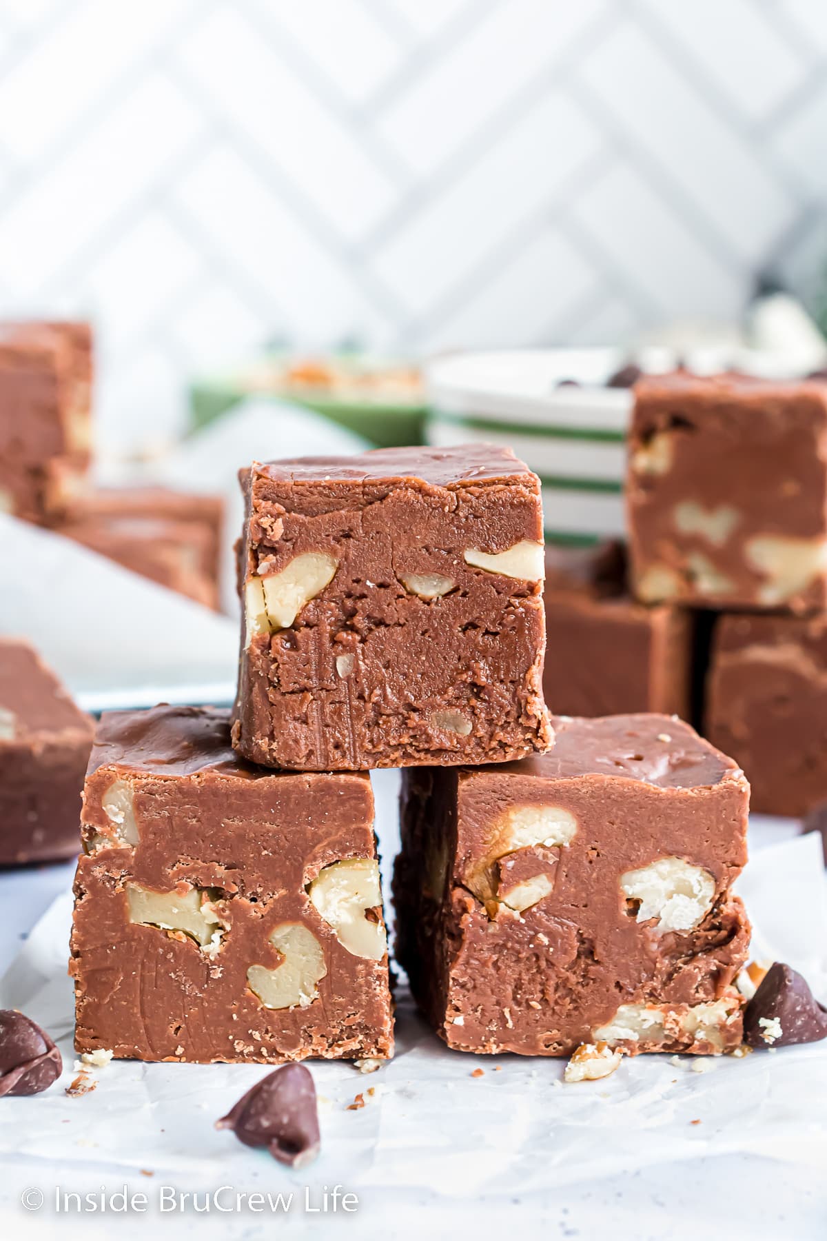 Three squares of chocolate walnut fudge stacked on a white board.