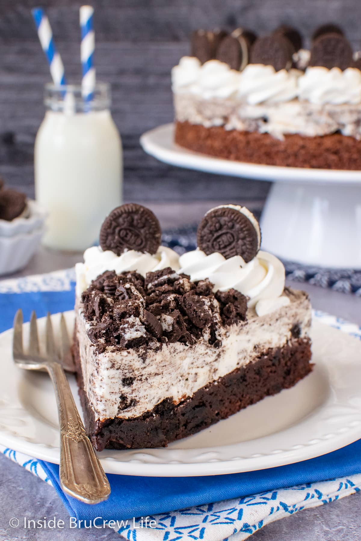 A slice of Oreo mousse cake on a white plate topped with Cool Whip and Oreo cookie chunks.
