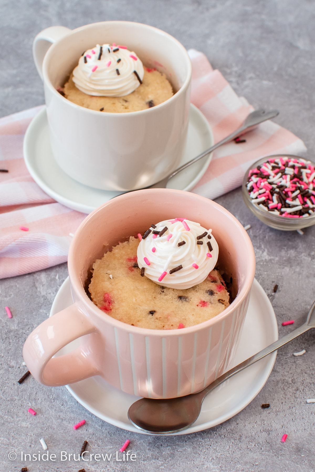 Two mug cakes with frosting on a gray board.