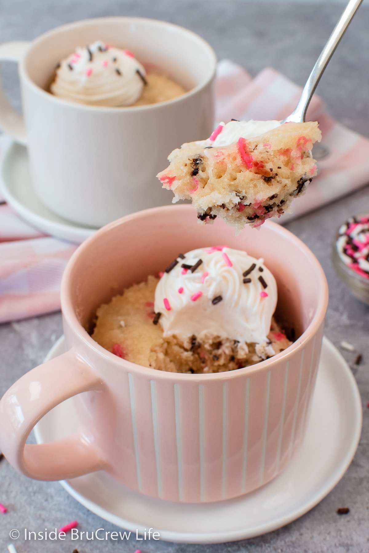 A pink mug with a cake baked in it and a spoon lifting a bite out.