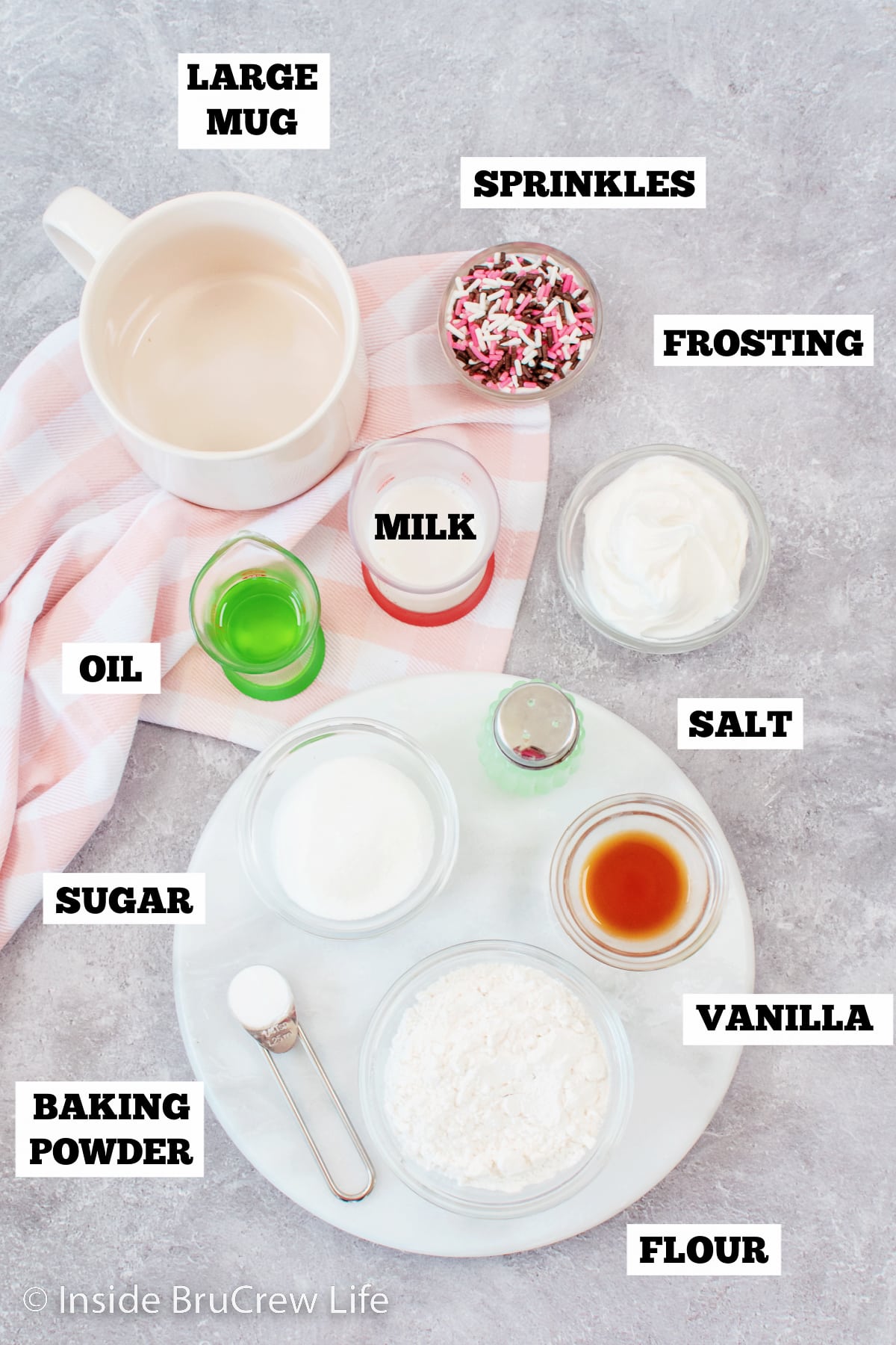 A gray board with ingredients needed to make a mug cake recipe.