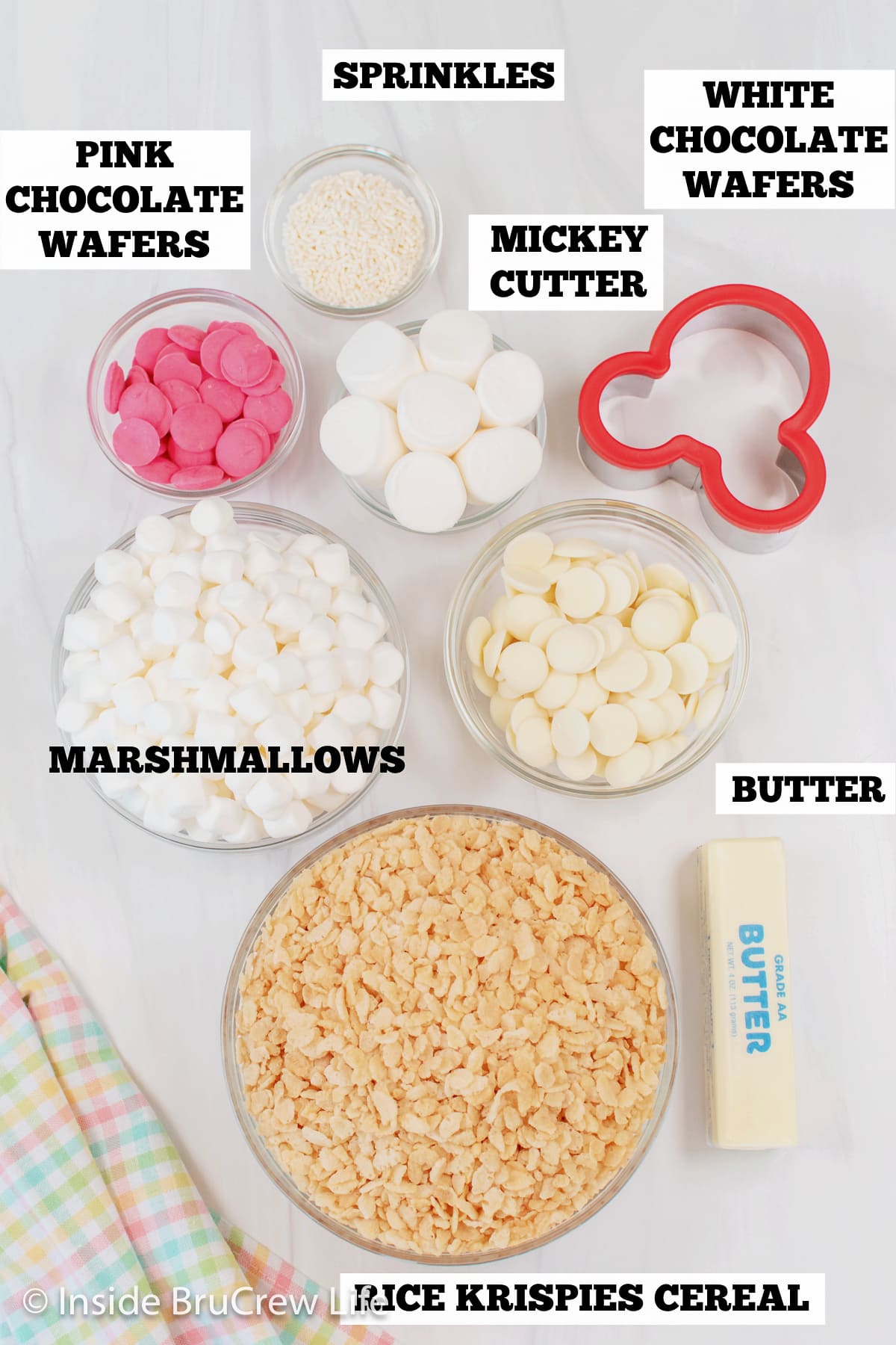 A white board with bowls of ingredients needed to make bunny rice krispie treats.