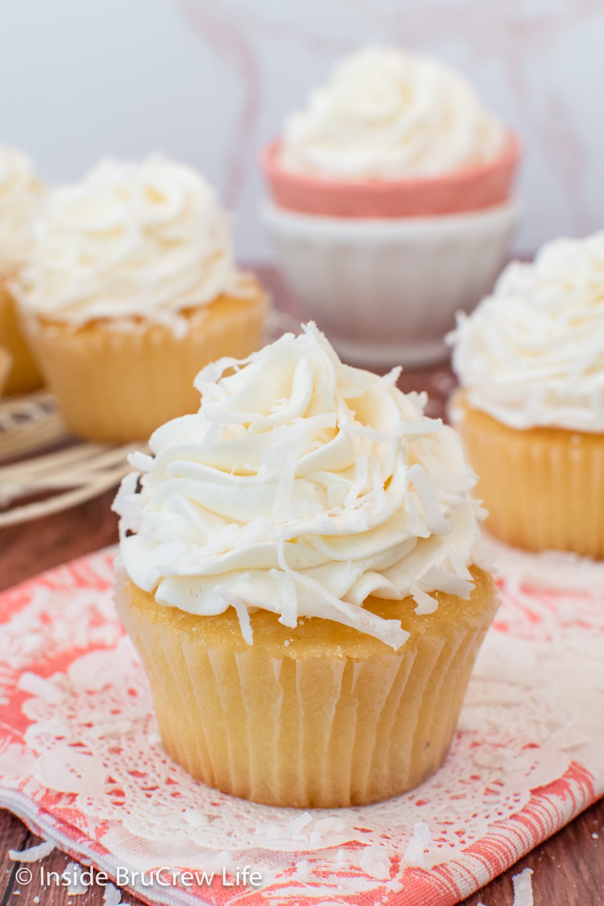 Three vanilla cupcakes topped with a swirl of coconut frosting and shredded coconut.