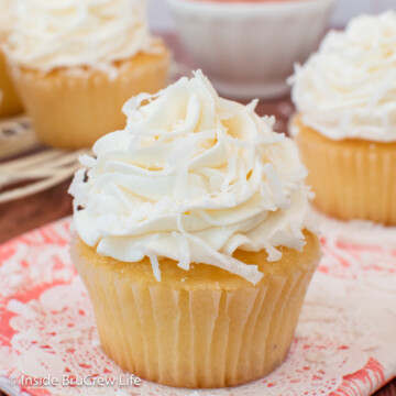 Three vanilla cupcakes topped with a swirl of coconut frosting and shredded coconut.