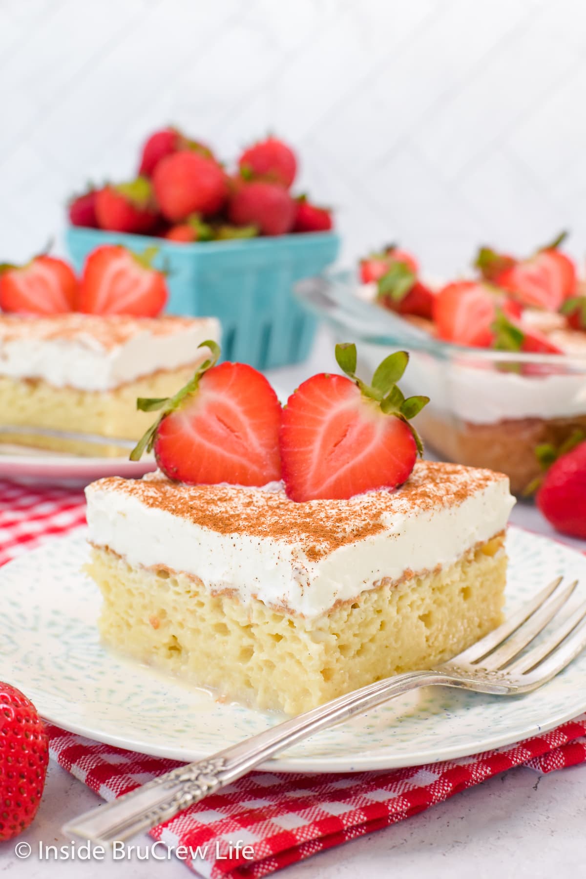 A slice of tres leches cake with strawberries on a white plate.