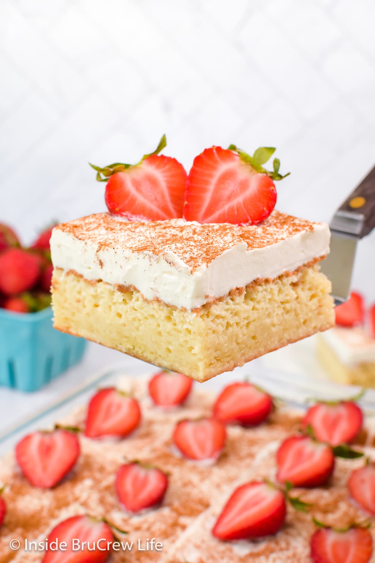 A piece of cake with whipped cream and strawberries being lifted out of a pan.