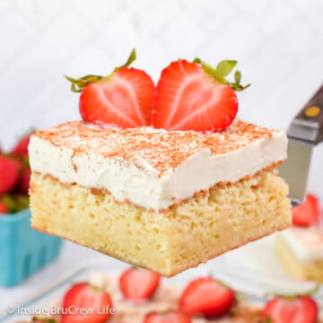 A piece of cake with whipped cream and strawberries being lifted out of a pan.