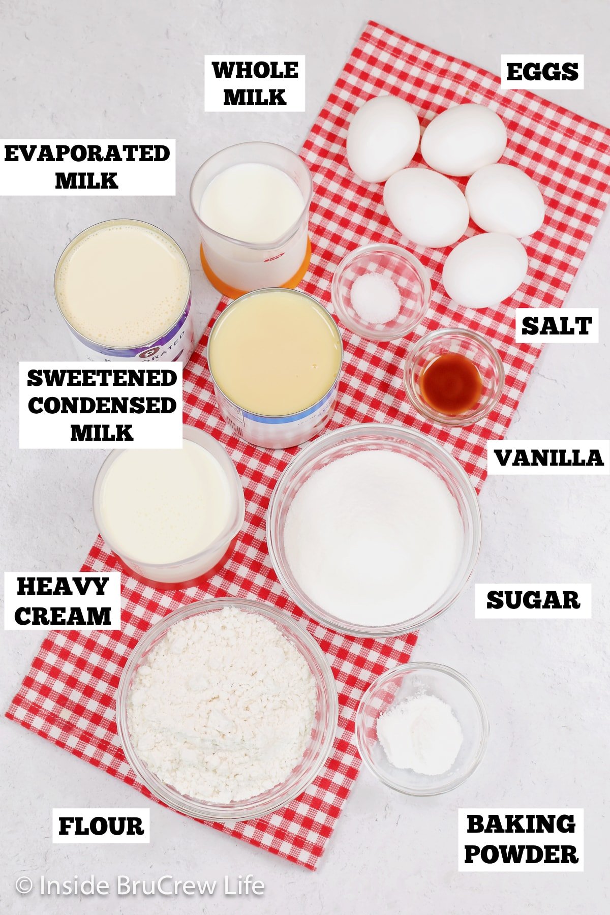 A white board with bowls of ingredients needed to make a milk soaked sponge cake.