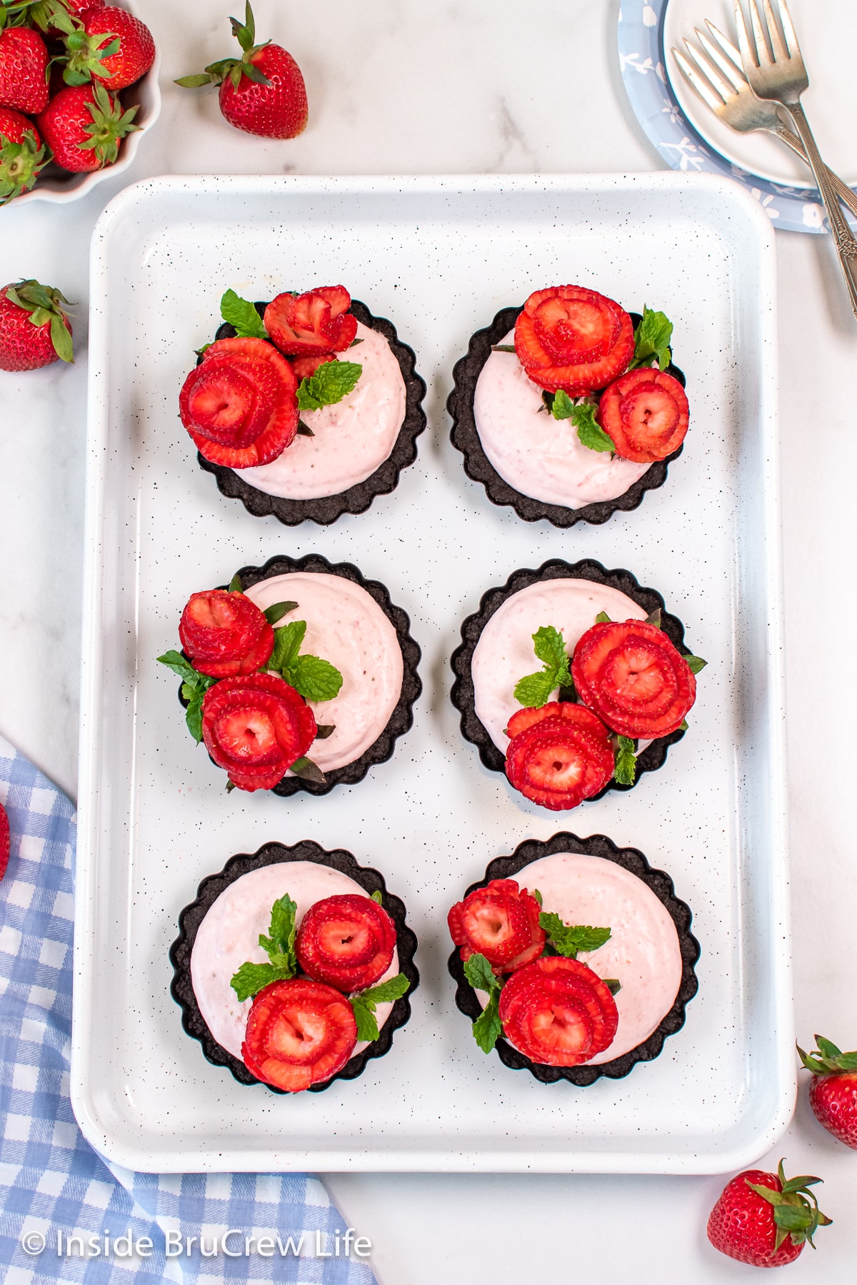 Six mini strawberry tarts topped with berries on a white pan.