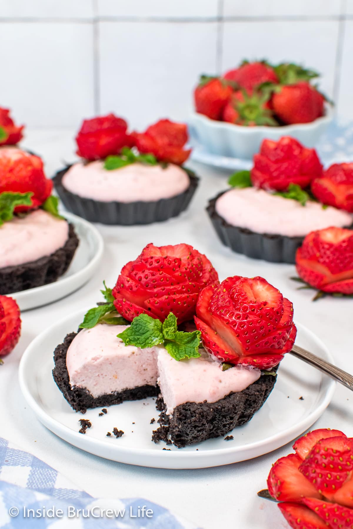 A pink strawberry tart with Oreo crust on white plates.
