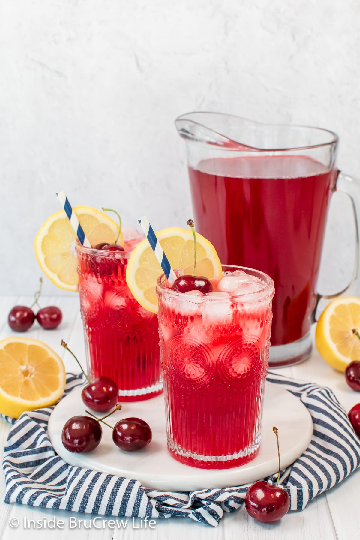 Two clear glasses filled with a red cherry lemonade and a lemon slice.
