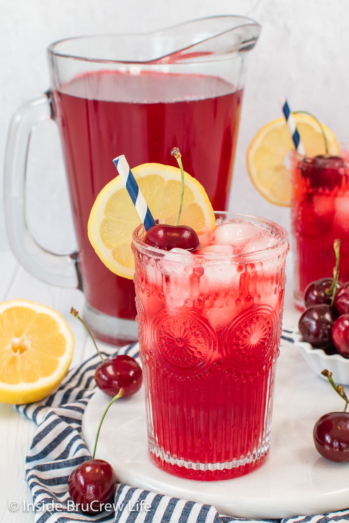 A clear glass with cherry drink and lemon slice.