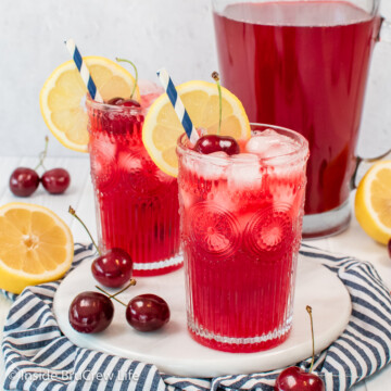 Two clear glasses filled with a red cherry lemonade and a lemon slice.