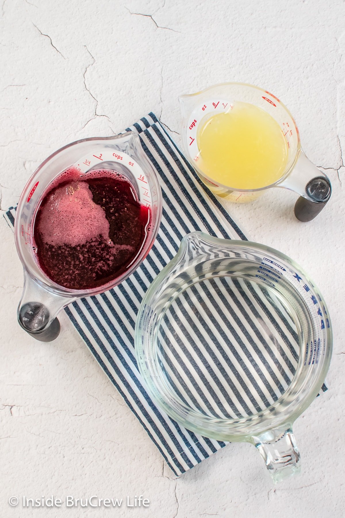 Three measuring cups with lemon and cherry juice and water.