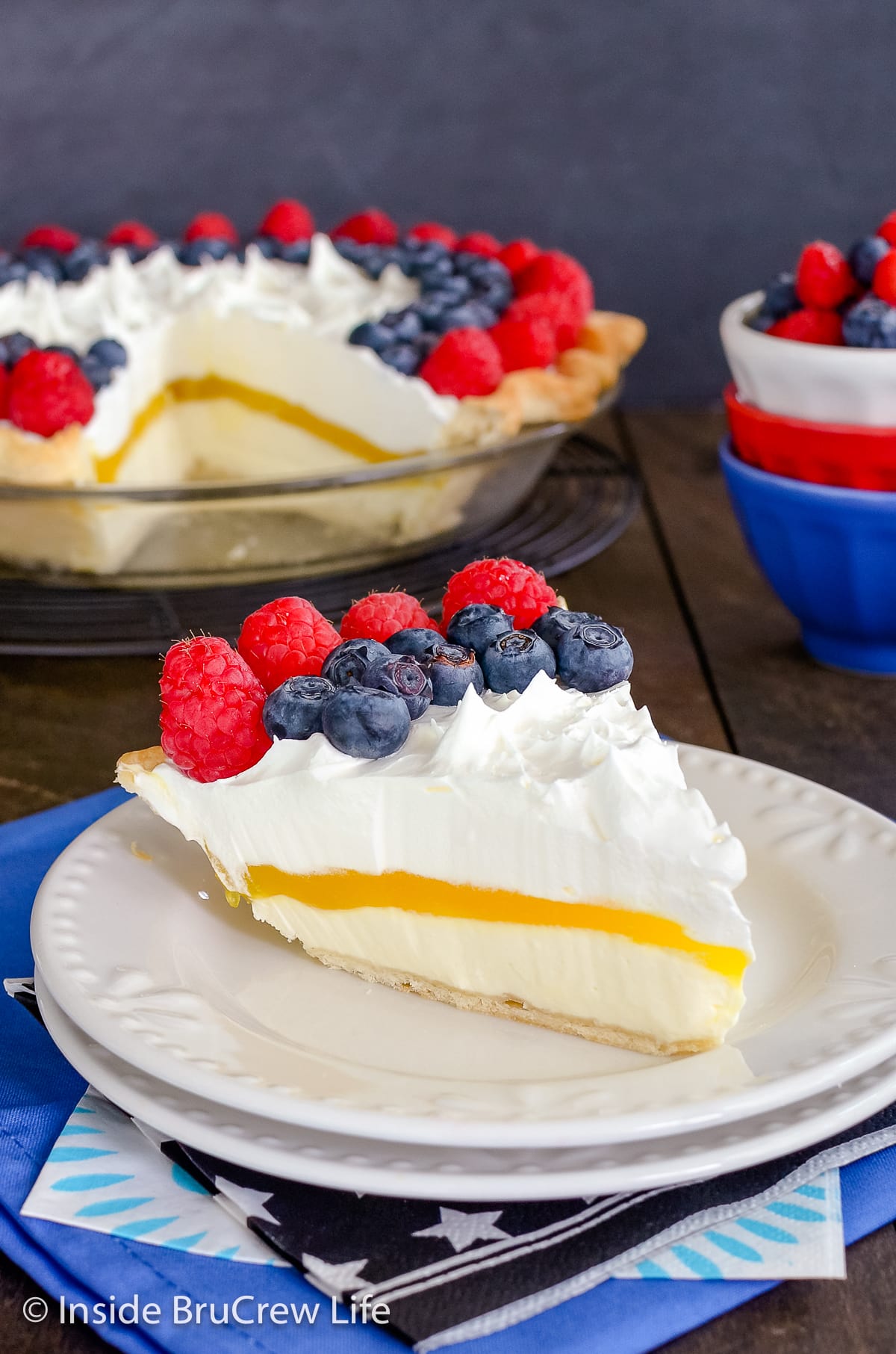 A white plate with a slice of pie topped with blueberries and raspberries on it.