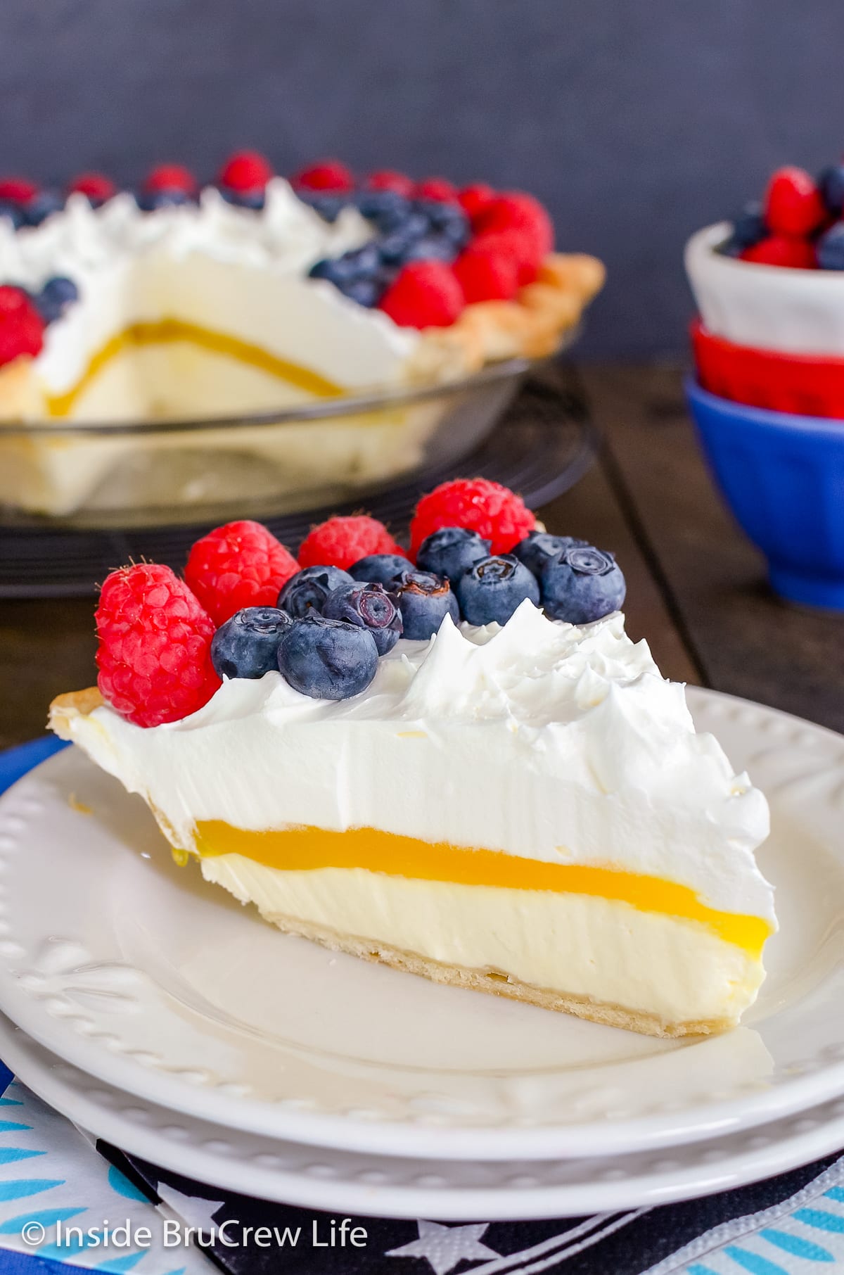 A slice of lemon pie topped with berries on a white plate.
