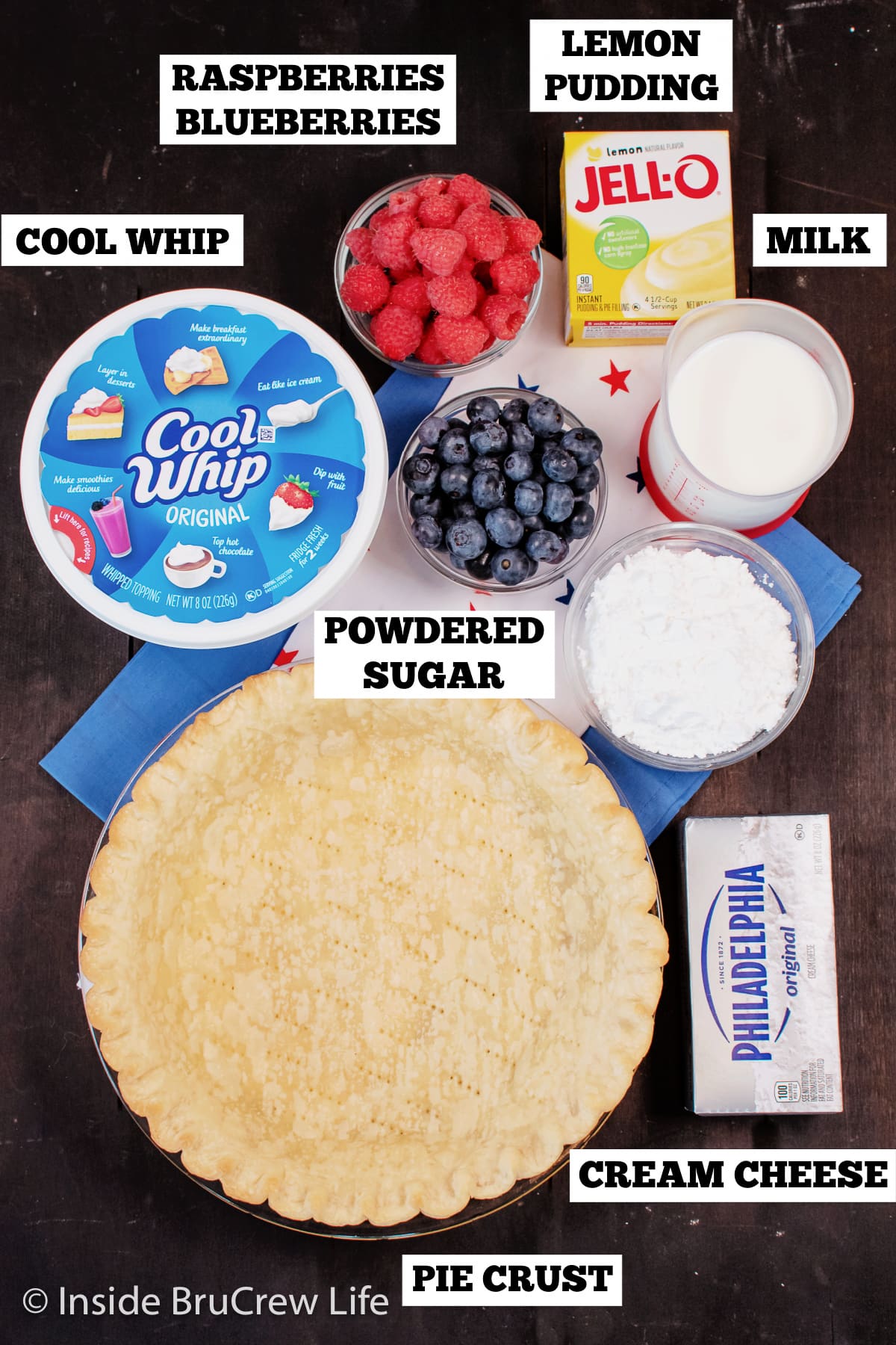 A brown board with bowls of ingredients needed to make a cream cheese pie.
