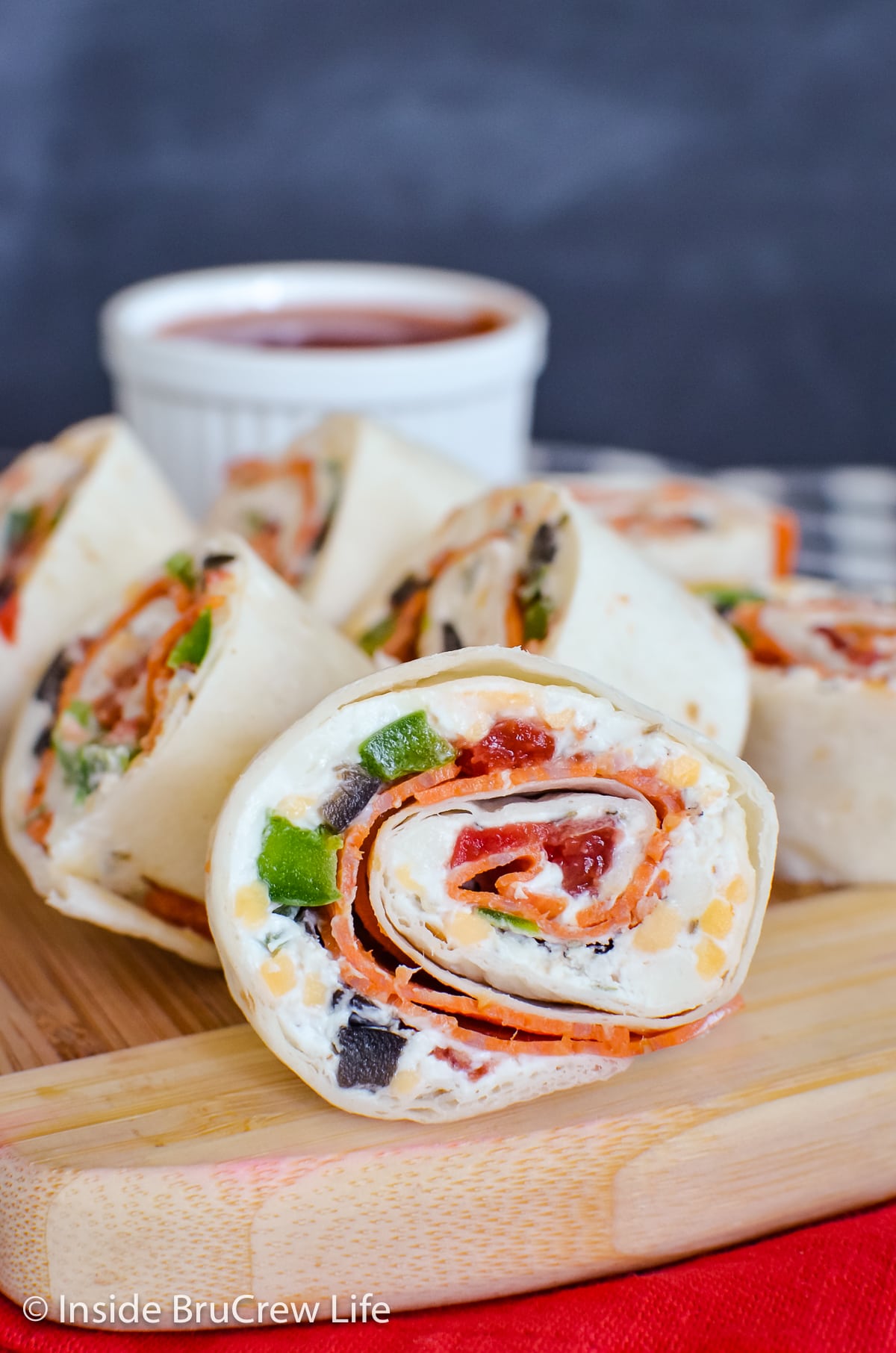 A stack of cream cheese tortilla rolls on a wooden board.