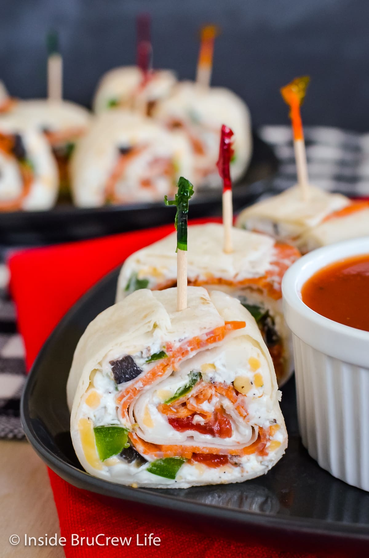 Three pizza roll ups on a plate with a bowl of pizza sauce.