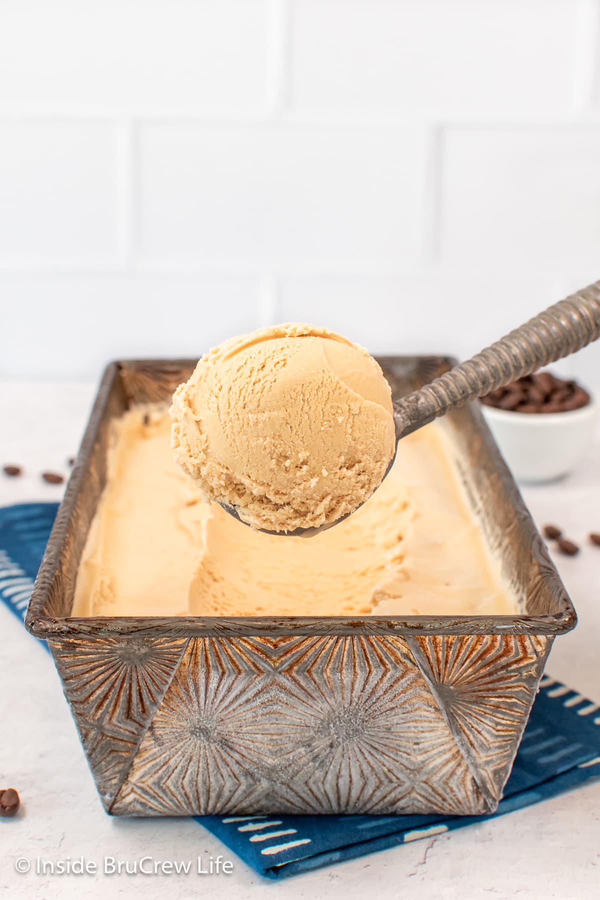 An ice cream scooper lifting a scoop of ice cream out of a pan.