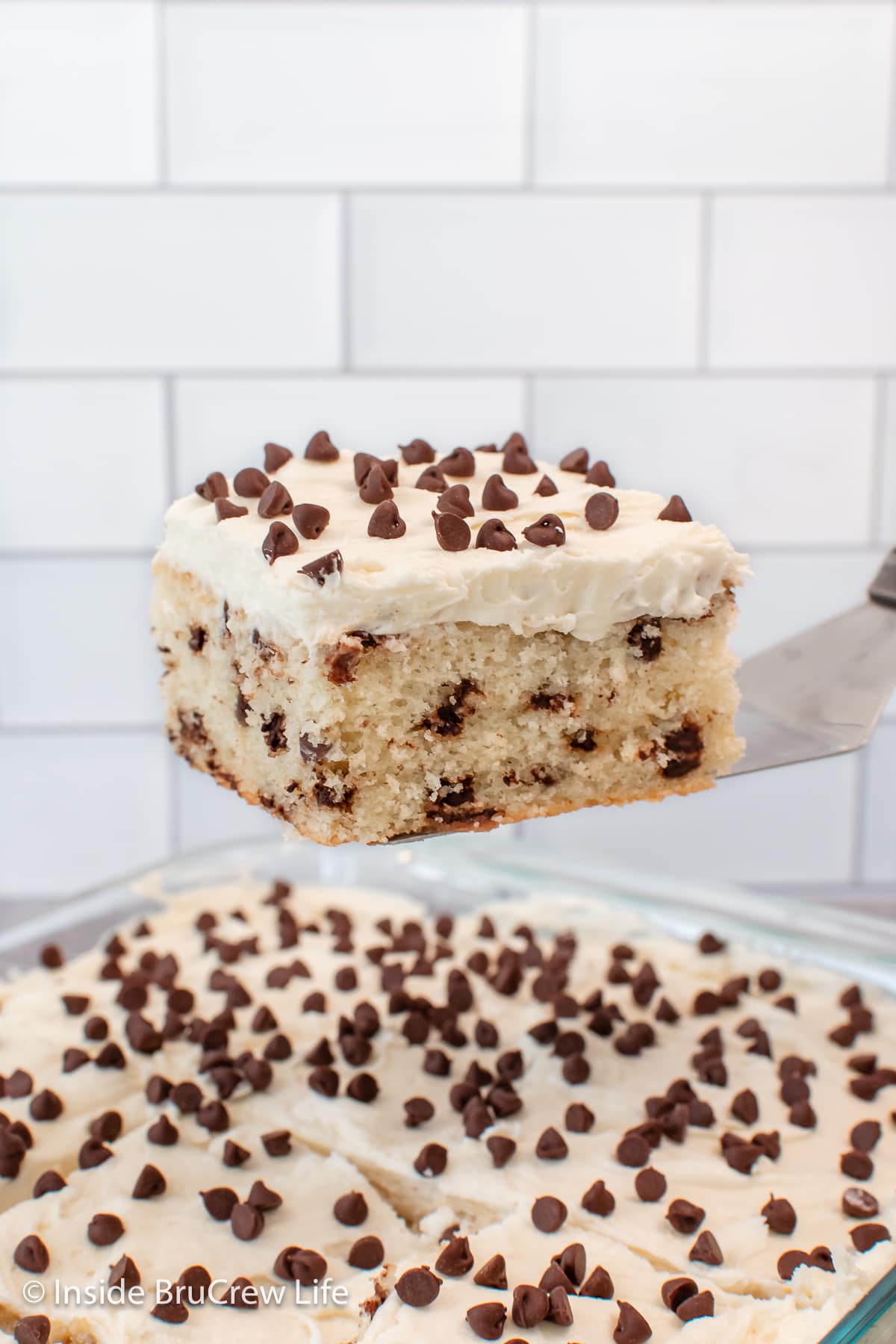 A spatula holding a slice of frosted cake above the cake pan.