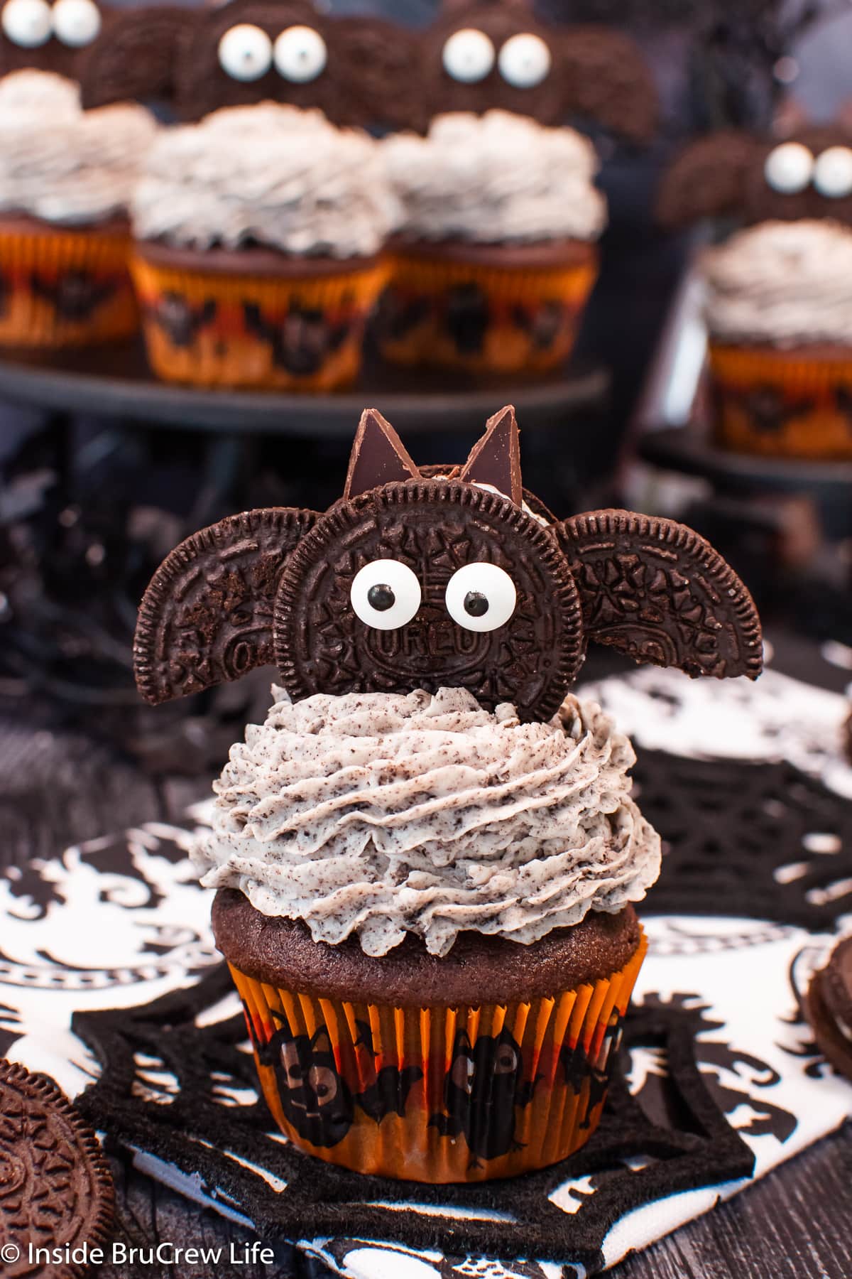 A frosted cupcake topped with a cookie decorated like a bat.