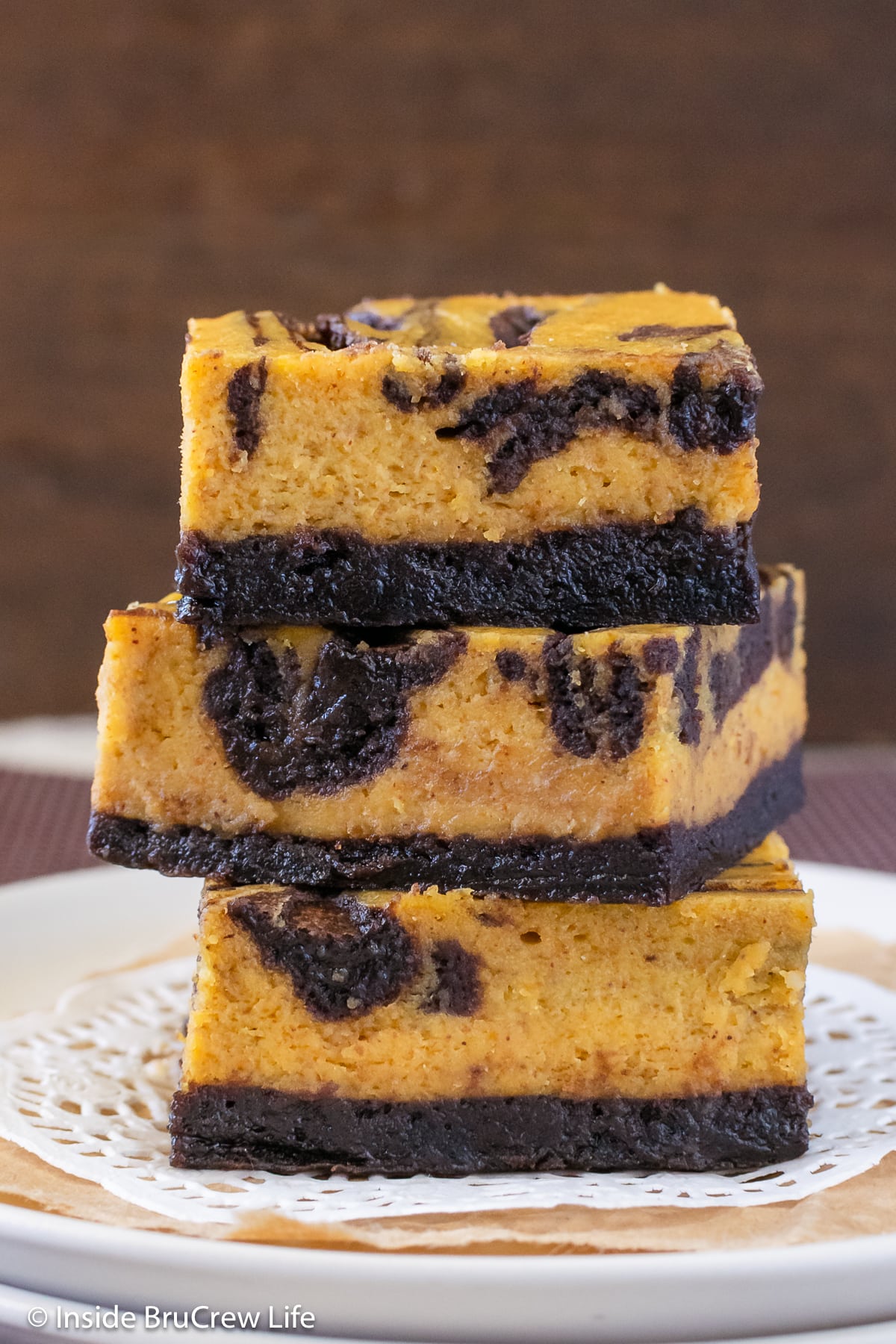 Three pumpkin cheesecake bars stacked on a plate.