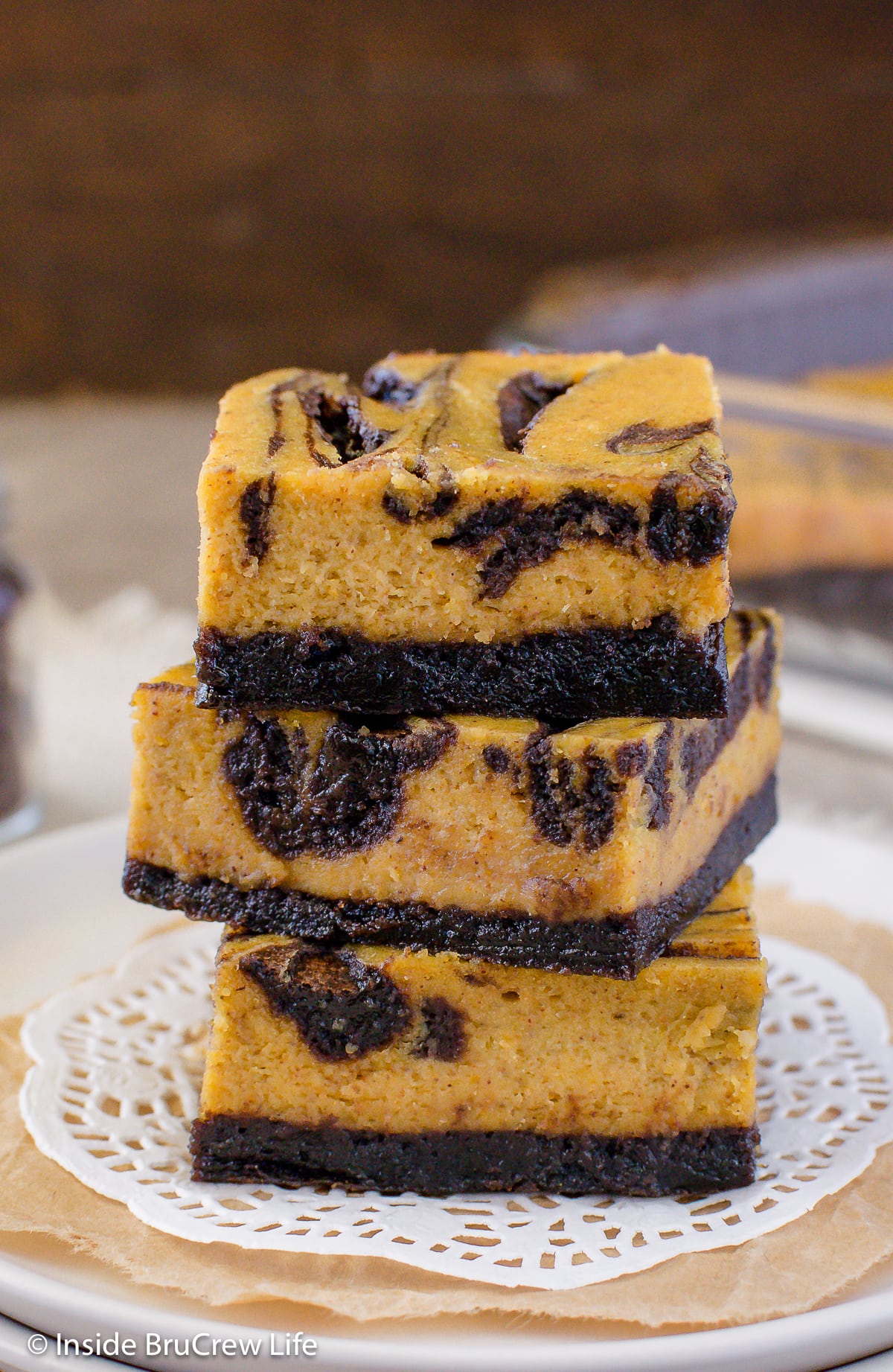 A stack of pumpkin cheesecake bars with brownie swirls on a plate.