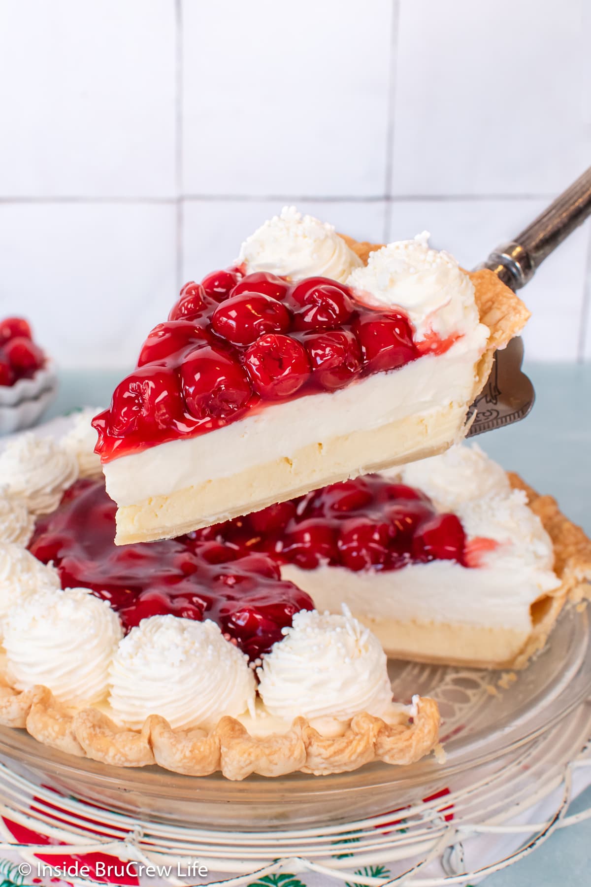 A piece of cream cheese pie with cherries being lifted out of the pan.