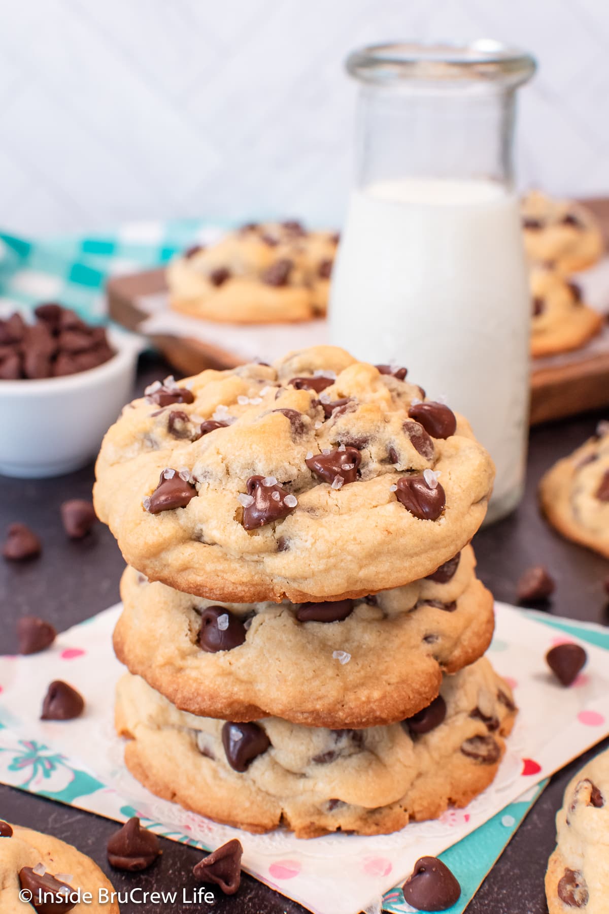 A stack of three puffy chocolate chip cookies on a napkin.
