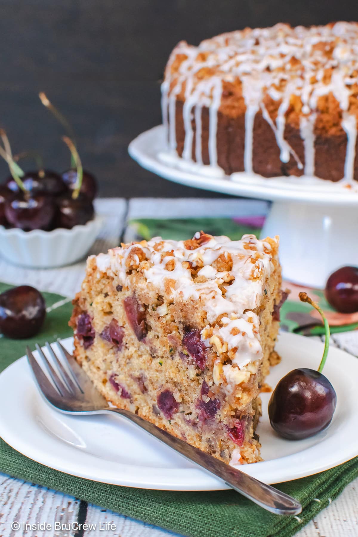 A slice of zucchini coffee cake with cherries on a white plate.