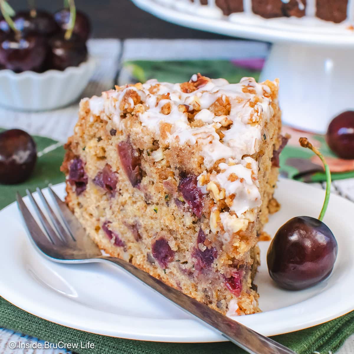 A slice of zucchini coffee cake with cherries on a white plate.