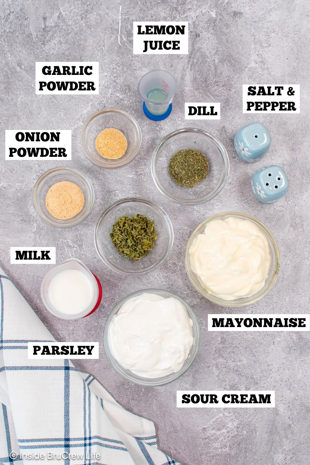 A gray board with bowls of ingredients needed to make ranch sauce.